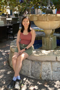 Peer Educator with tank top and green short smiling to camera while sitting on water fountain